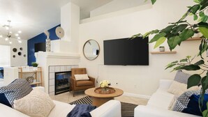 A living room with a fireplace, a TV mounted on the wall, and a coffee table with flowers. - Quiet 4 BD Home w/ Pool (North Las Vegas)