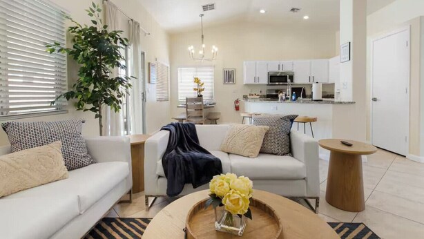 A modern living room with a sofa, coffee table, and a dining area in the background. - Quiet 4 BD Home w/ Pool (North Las Vegas)