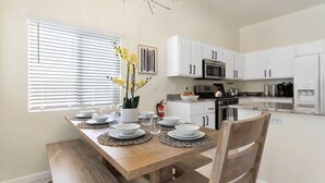 A dining area with a wooden table set for four, white cabinets, a microwave, and a stove in the adjacent kitchen. - Quiet 4 BD Home w/ Pool (North Las Vegas)
