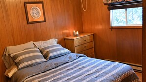 A bedroom with a wooden ceiling, a bed with striped bedding, a nightstand, a framed picture, and a window with a floral curtain. - Family Reunion Cottage - Can sleep 16+  - Includes Motor Boat, Canoe, AC - Wi-Fi (Britt)