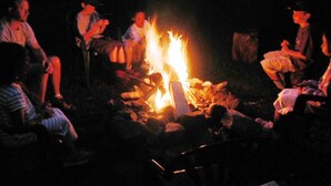 A group of people sitting around a campfire in a dark outdoor setting. - Family Reunion Cottage - Can sleep 16+  - Includes Motor Boat, Canoe, AC - Wi-Fi (Britt)