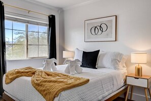 Een hotelkamer met een bed, twee bedlampen, een lijst met een kunstwerk en een raam met gordijnen.