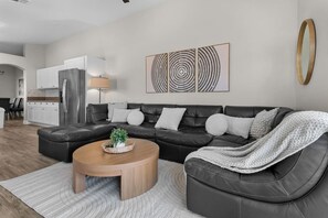 A modern living room with a sectional sofa, a wooden coffee table, and a kitchen in the background.