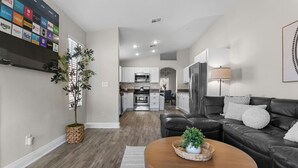 A modern living room with a leather sofa, a wooden coffee table, and a kitchen in the background. - Modern 5 BD Home w/ Smart TV and Ping Pong (North Las Vegas)