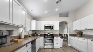 A modern kitchen with white cabinets, a microwave, a stove, and a dishwasher. - Modern 5 BD Home w/ Smart TV and Ping Pong (North Las Vegas)