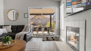 A living room with a fireplace, a sofa, a coffee table, and a sliding glass door leading to a patio. - Modern 5 BD Home w/ Smart TV and Ping Pong (North Las Vegas)