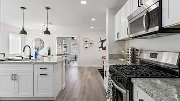 A modern kitchen with white cabinets, a stainless steel microwave, a gas stove, and pendant lighting.