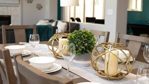 A dining table set with white plates, bowls, and wine glasses, surrounded by chairs.