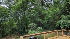 Eine Holzterrasse mit Grill, umgeben von dichtem Wald.