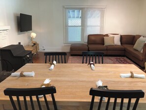 Un coin repas avec une table en bois, des chaises noires, un canapé marron et un téléviseur fixé au mur.