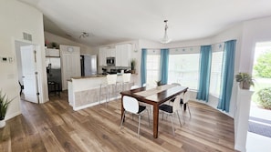 A modern kitchen with a central island, white cabinetry, and a dining area with a wooden table and chairs. - Pool & Beach – Shark Teeth Hunting – Families welcome – heated Pool (Venice)
