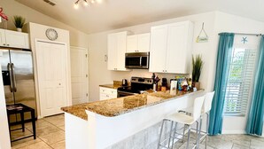 Una cocina moderna con armarios blancos, encimera de granito, electrodomésticos de acero inoxidable y una barra con taburetes.