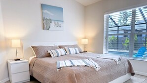 Un dormitorio con una cama grande, dos mesitas de noche con lámparas, una ventana con persianas y un cuadro en la pared.