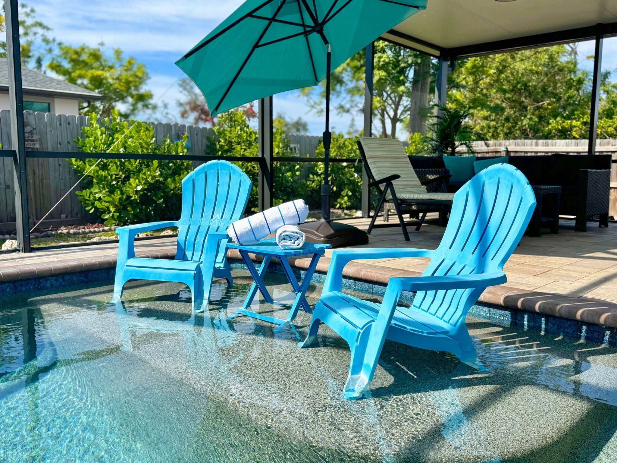 Un espace piscine avec deux chaises Adirondack bleues, une table avec une serviette et un parasol vert.