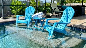 Un área de piscina con dos sillas Adirondack azules, una mesa con una toalla y un paraguas verde.