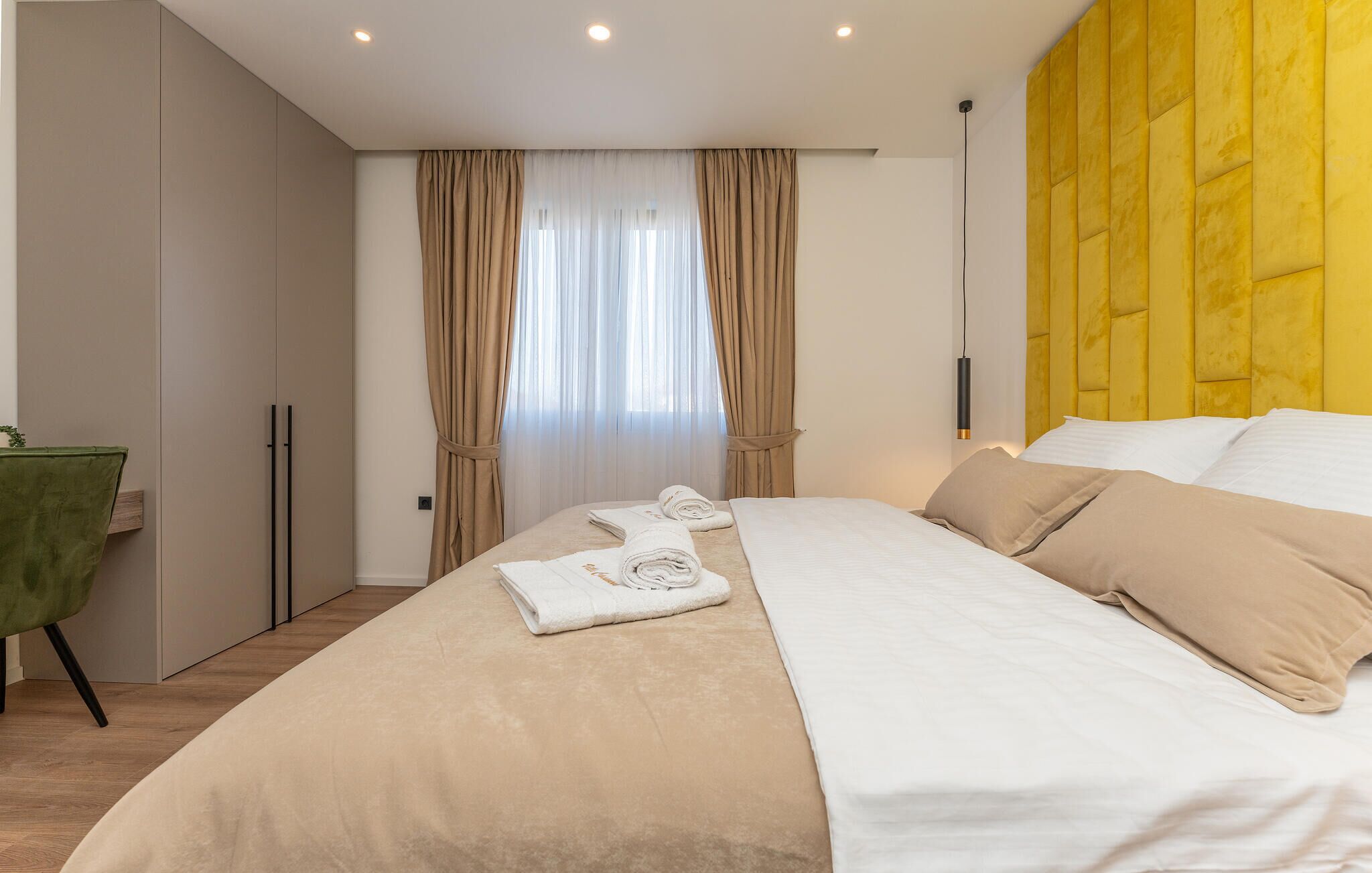 Een hotelkamer met een bed, een groene fauteuil, een kledingkast en een raam met gordijnen.