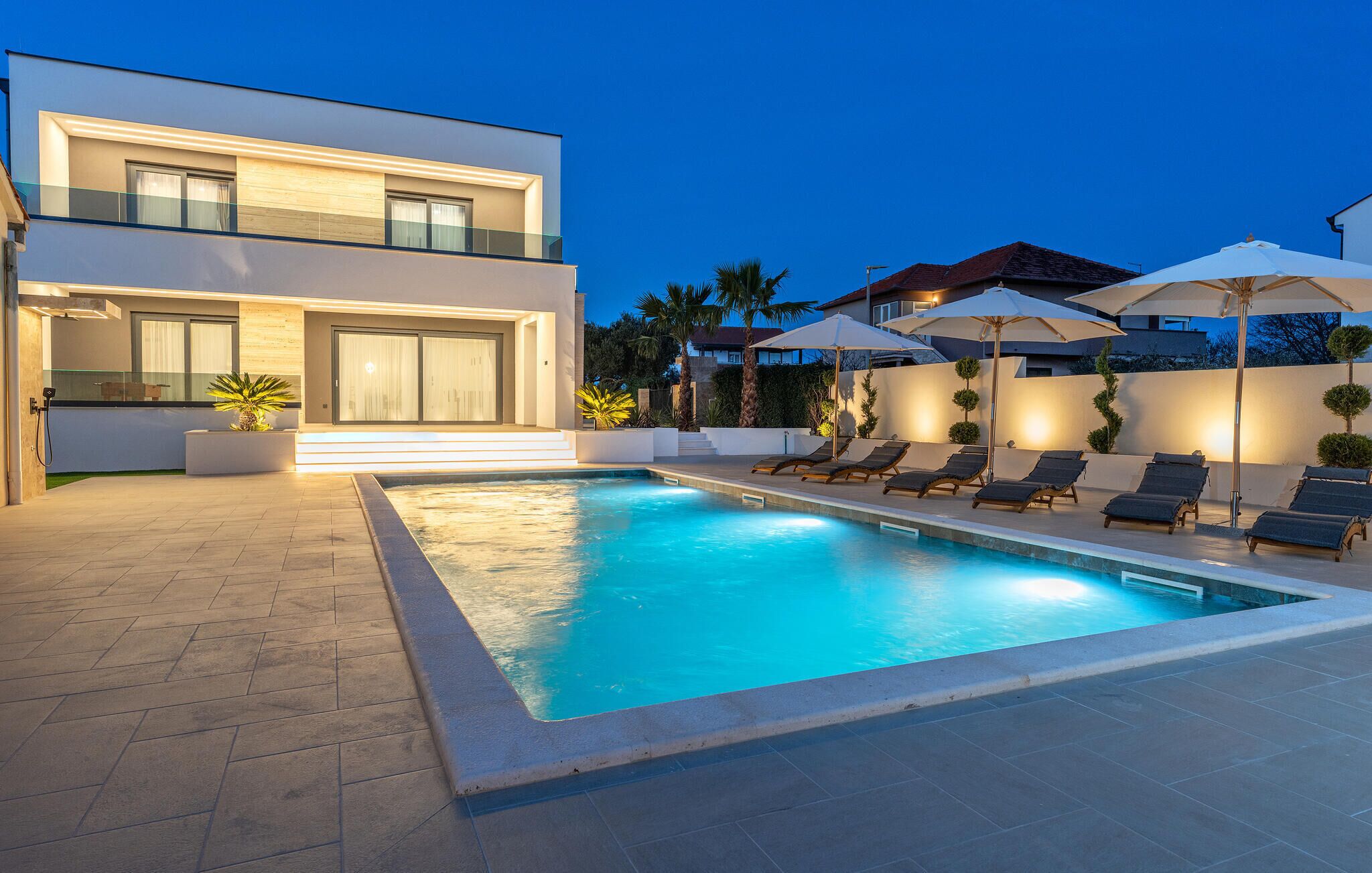 A modern two-story house with a swimming pool, outdoor seating, and a well-lit patio area.