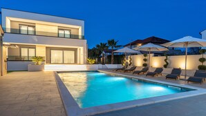 A modern two-story house with a swimming pool, outdoor seating, and a well-lit patio area.
