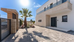 A modern building with a flat roof, large windows, and a paved courtyard with palm trees.