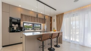 A modern kitchen with a central island, bar stools, and a view of greenery outside.