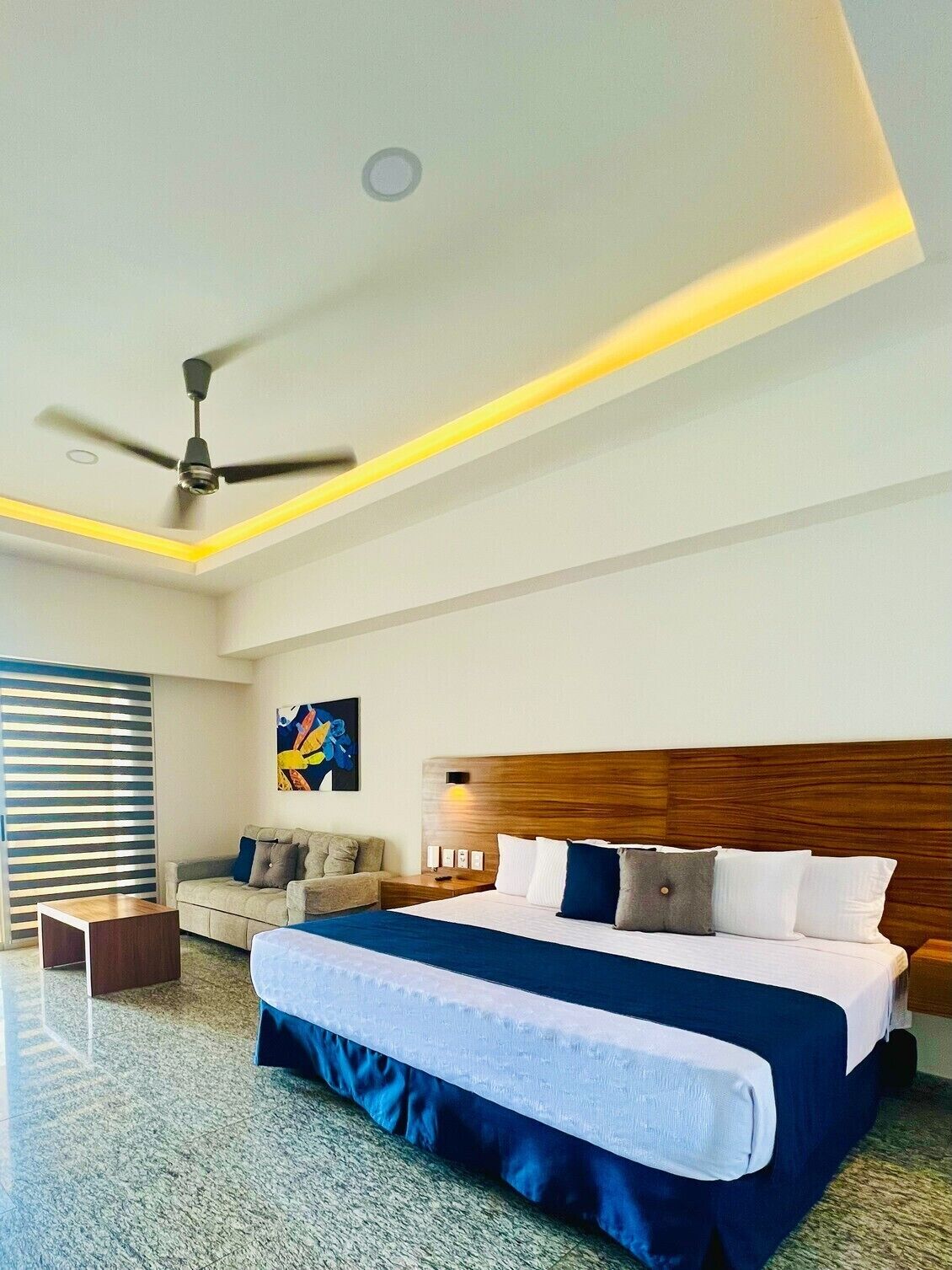 Una habitación de hotel moderna con una cama grande, un ventilador de techo y un cuadro en la pared.