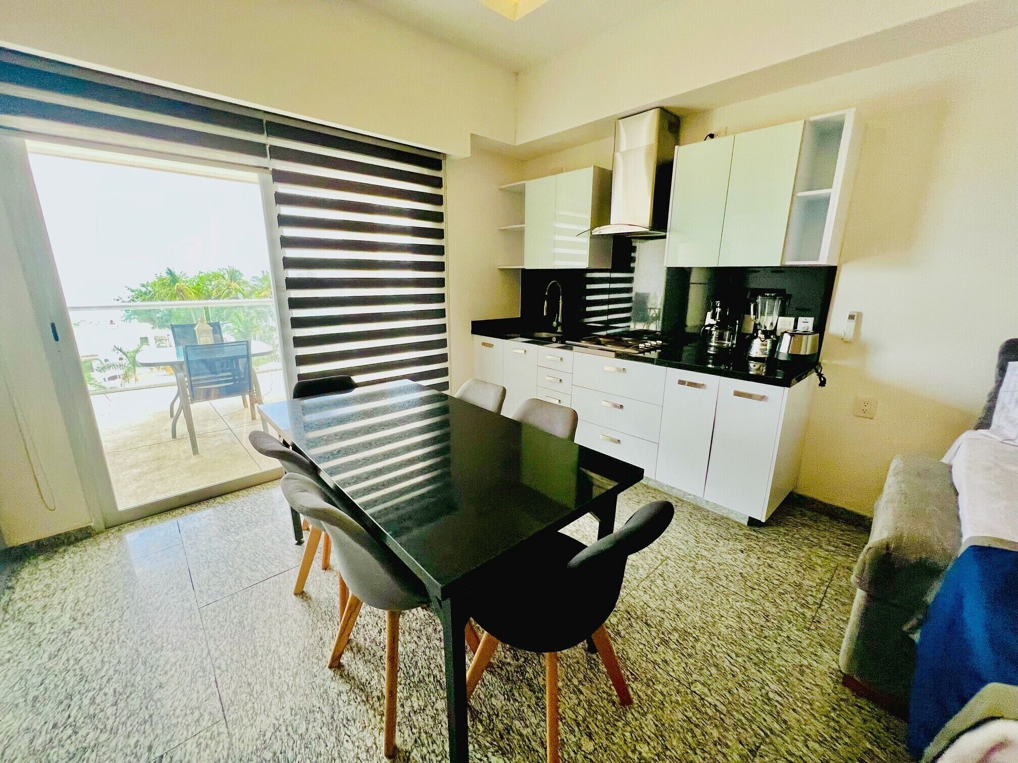 A modern kitchen with white cabinets, a black countertop, and a dining area with a glass door leading to a balcony.