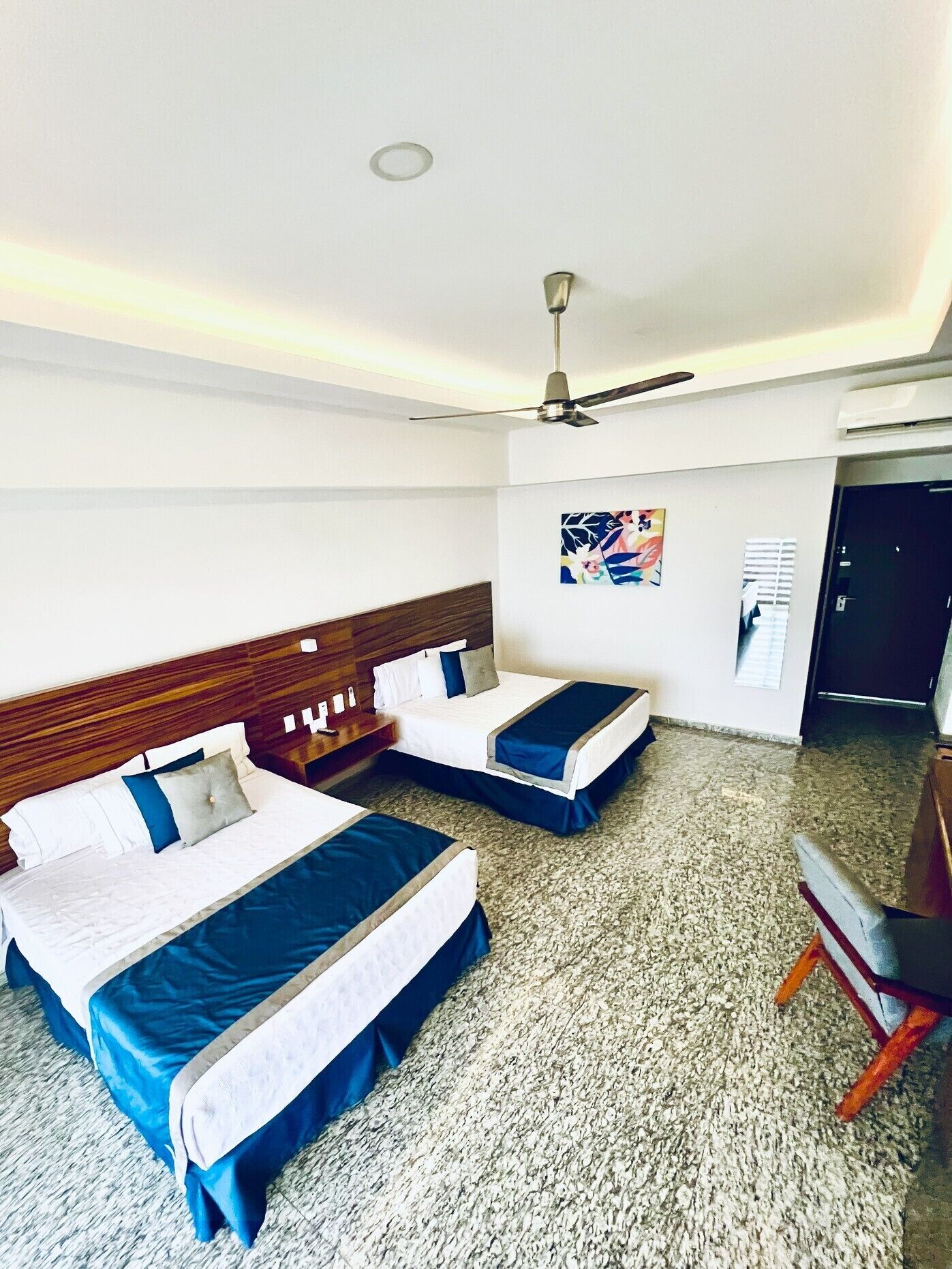 Habitación de hotel con dos camas, un ventilador de techo, un cuadro en la pared y piso alfombrado.