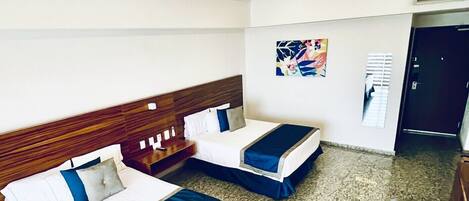 Habitación de hotel con dos camas, un ventilador de techo, un cuadro en la pared y piso alfombrado.