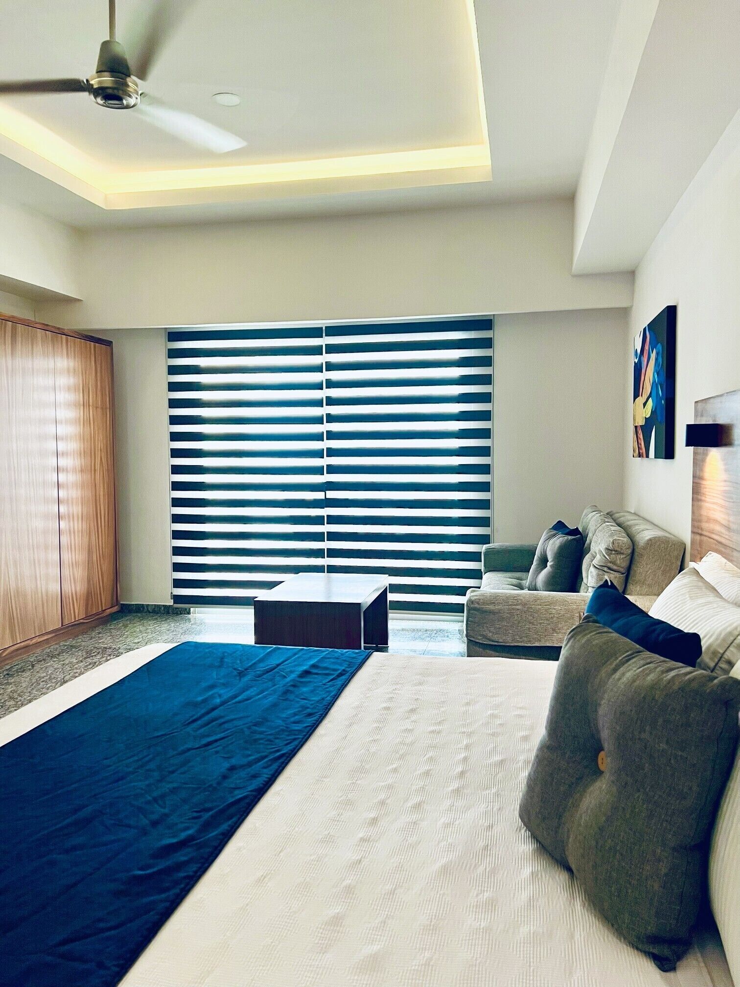 Un dormitorio moderno con una cama grande, un ventilador de techo y una ventana con persianas.