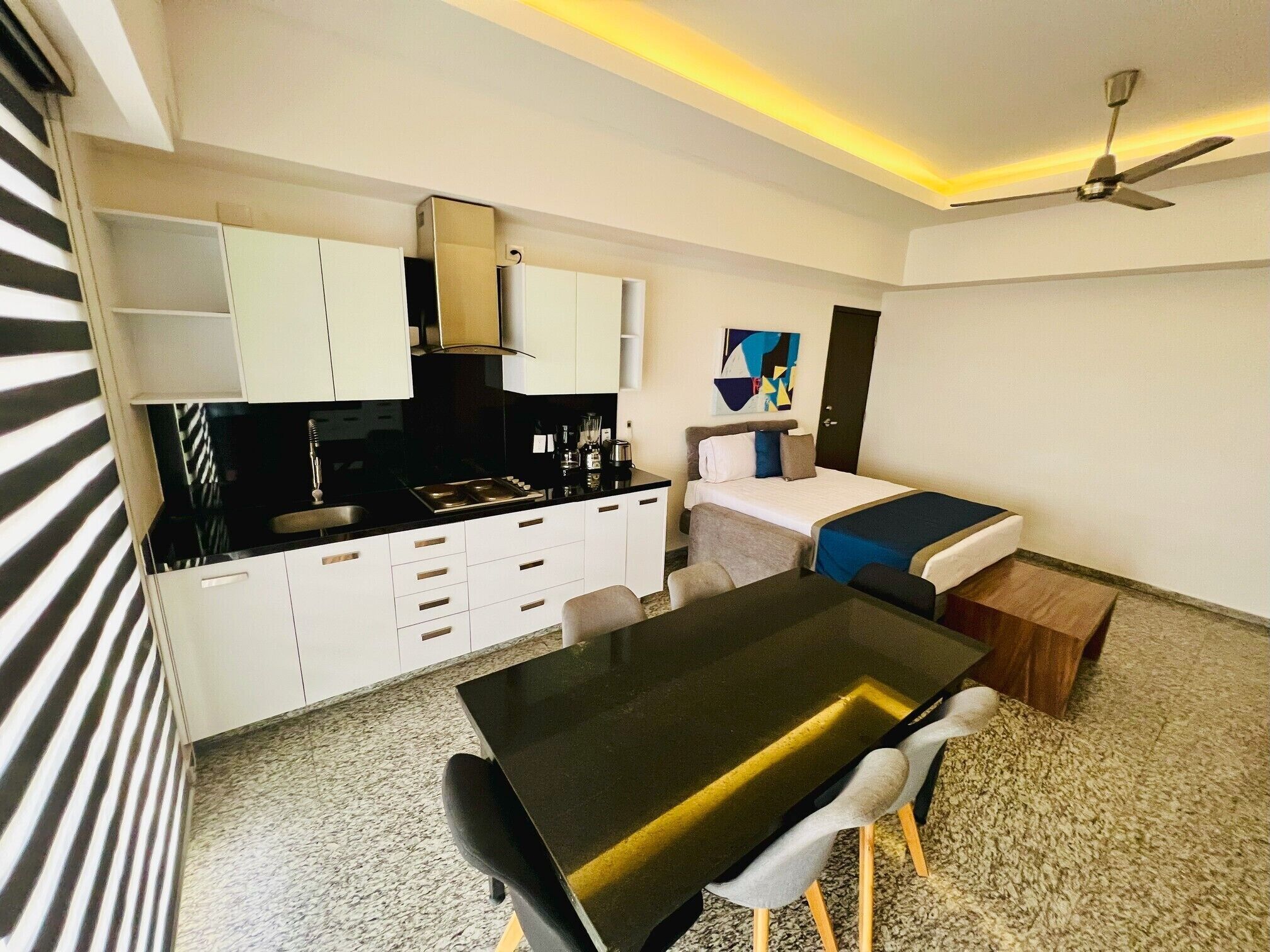 A compact hotel room with a kitchenette, a dining area, and a bed.