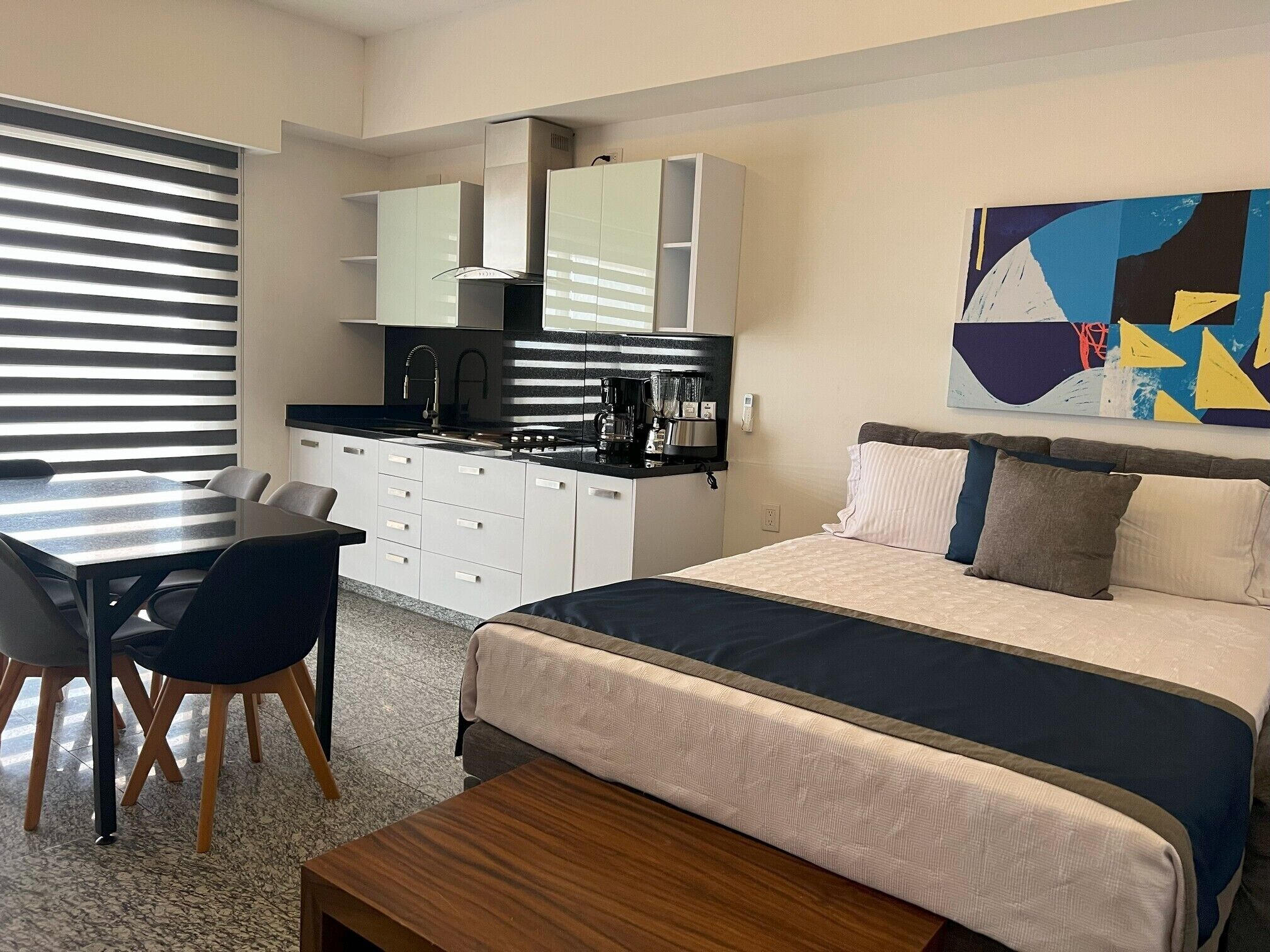 Ett modernt hotellrum med en säng, ett skrivbord och ett litet pentry.