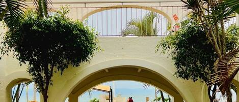 Un paseo techado con arcos que conduce a una zona de piscina con tumbonas y vistas al mar.