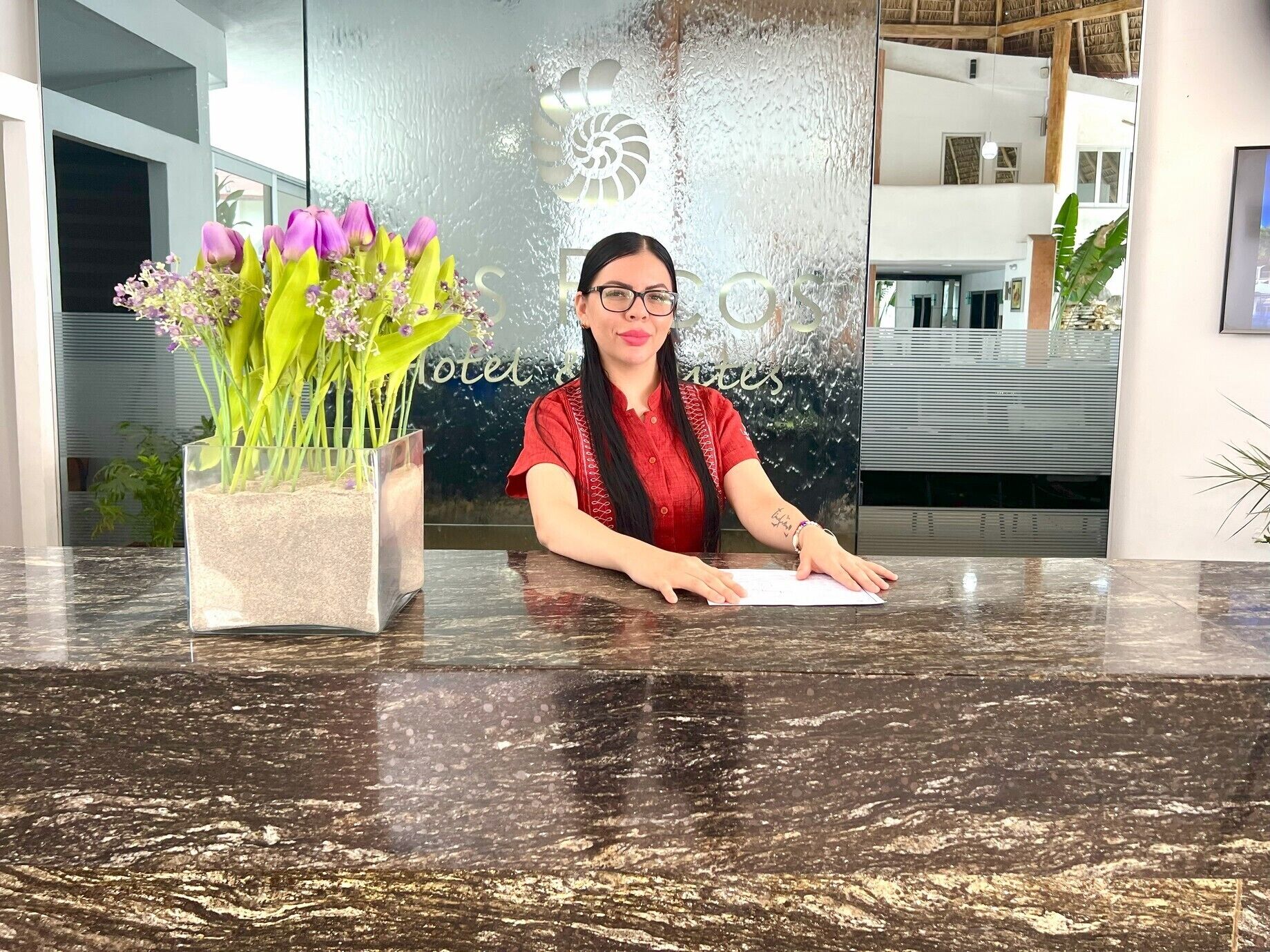 A reception desk with a vase of flowers, a glass wall with a logo, and a modern interior.