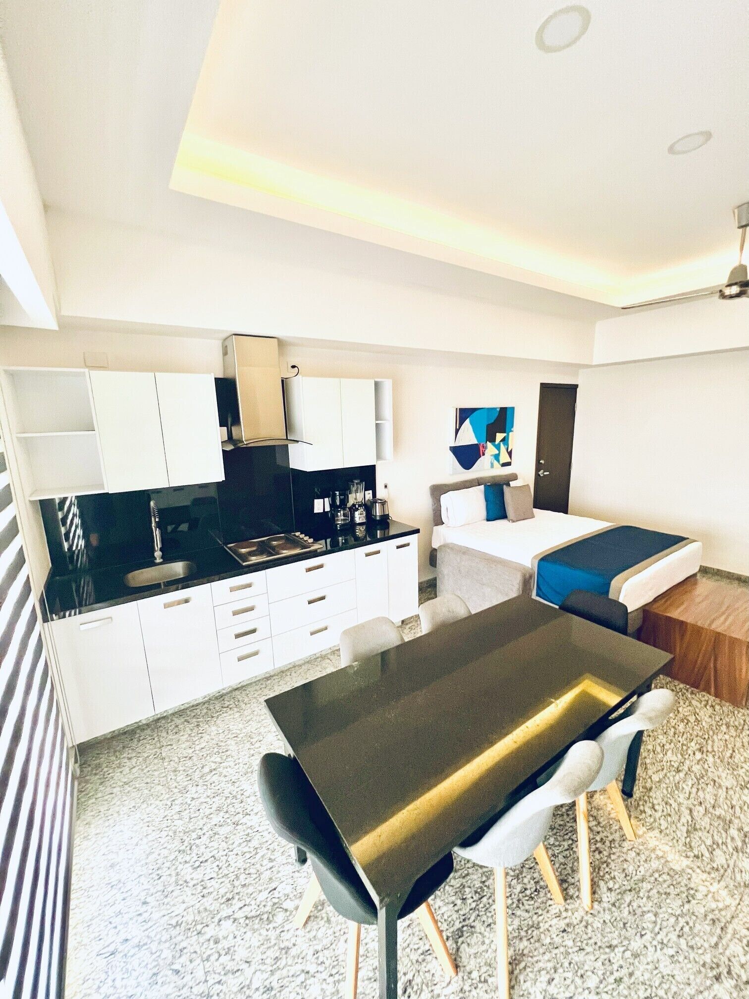 A modern hotel room with a kitchenette, a dining area, and a bed.
