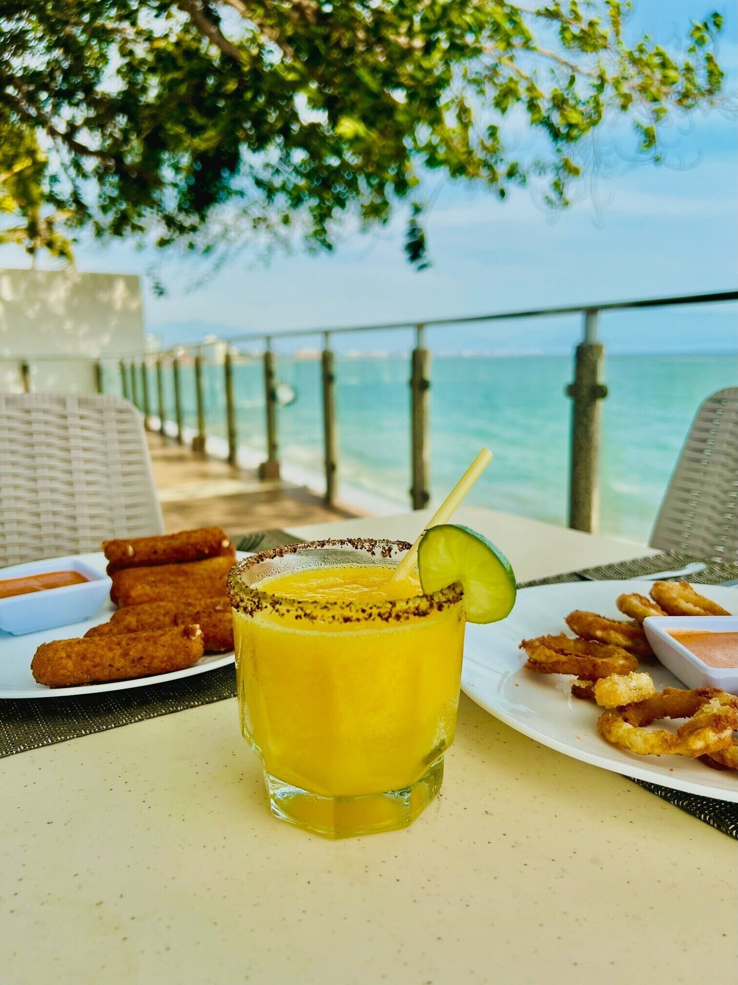 Ein Tisch mit einem Getränk, gebratenem Essen und Blick auf das Meer.