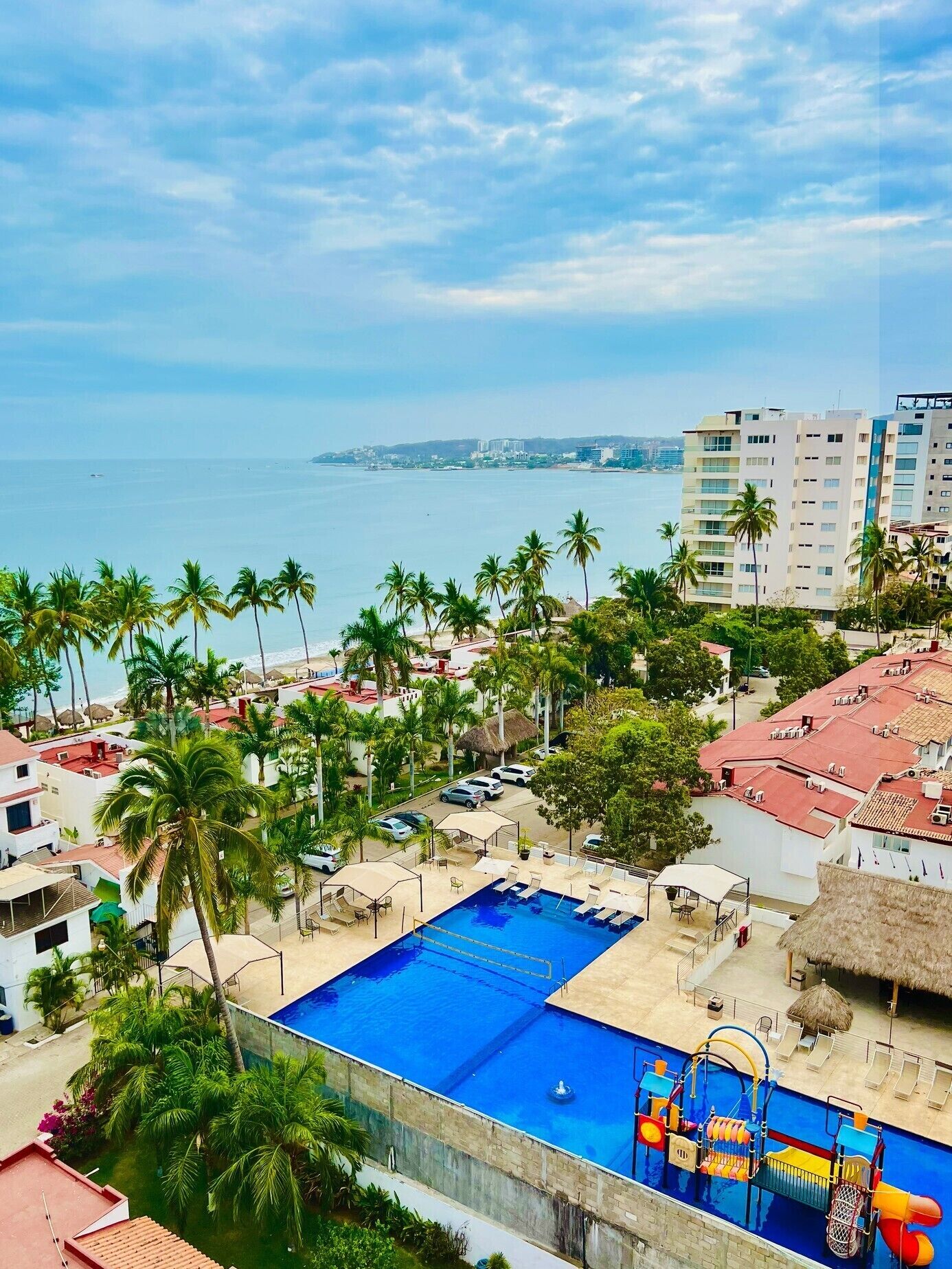 A resort with a large swimming pool, palm trees, and a view of the ocean.