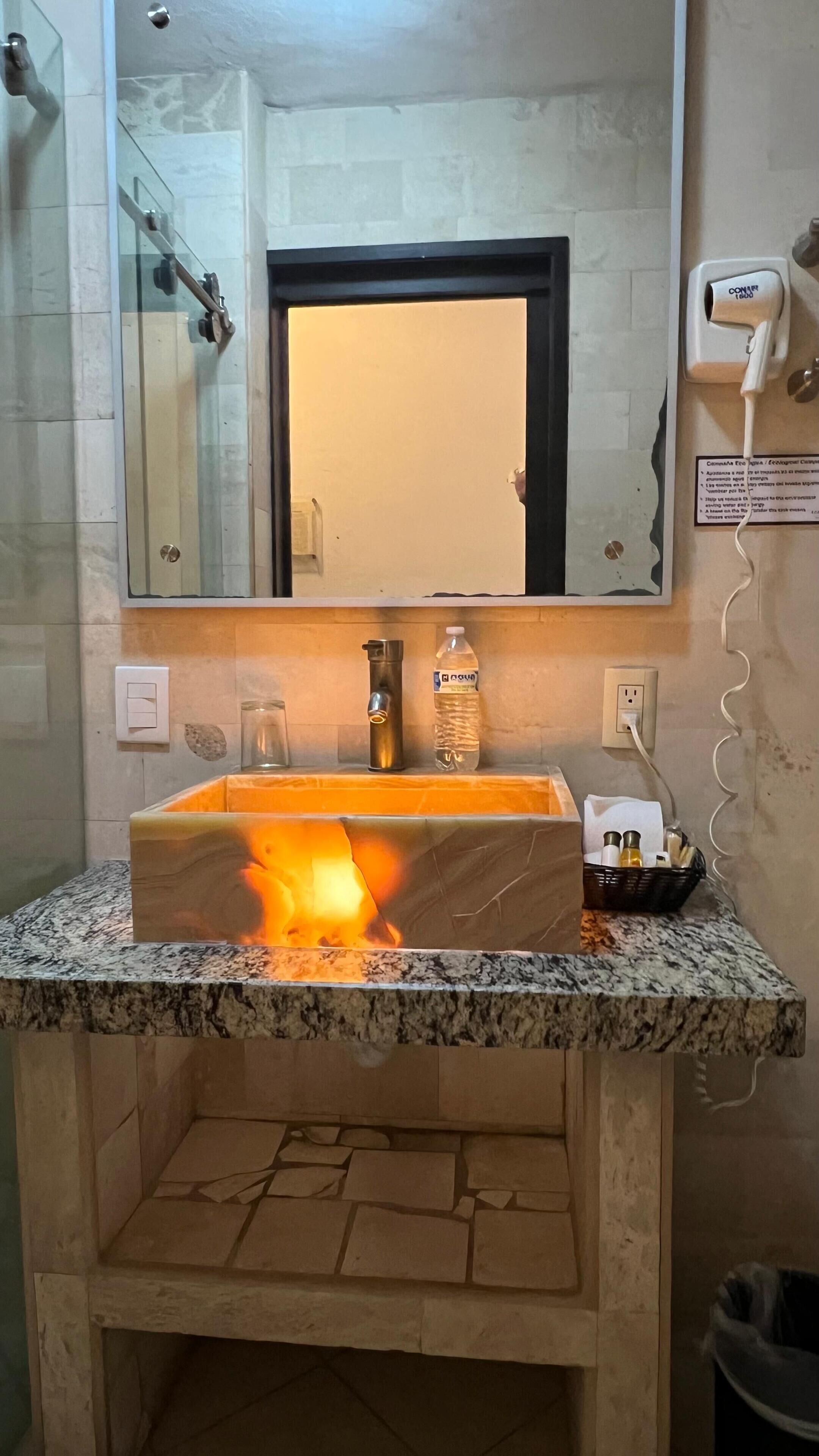 Ein Badezimmer mit Marmorplatte, Waschbecken, Spiegel, Handtuchspender und einer Wasserflasche.