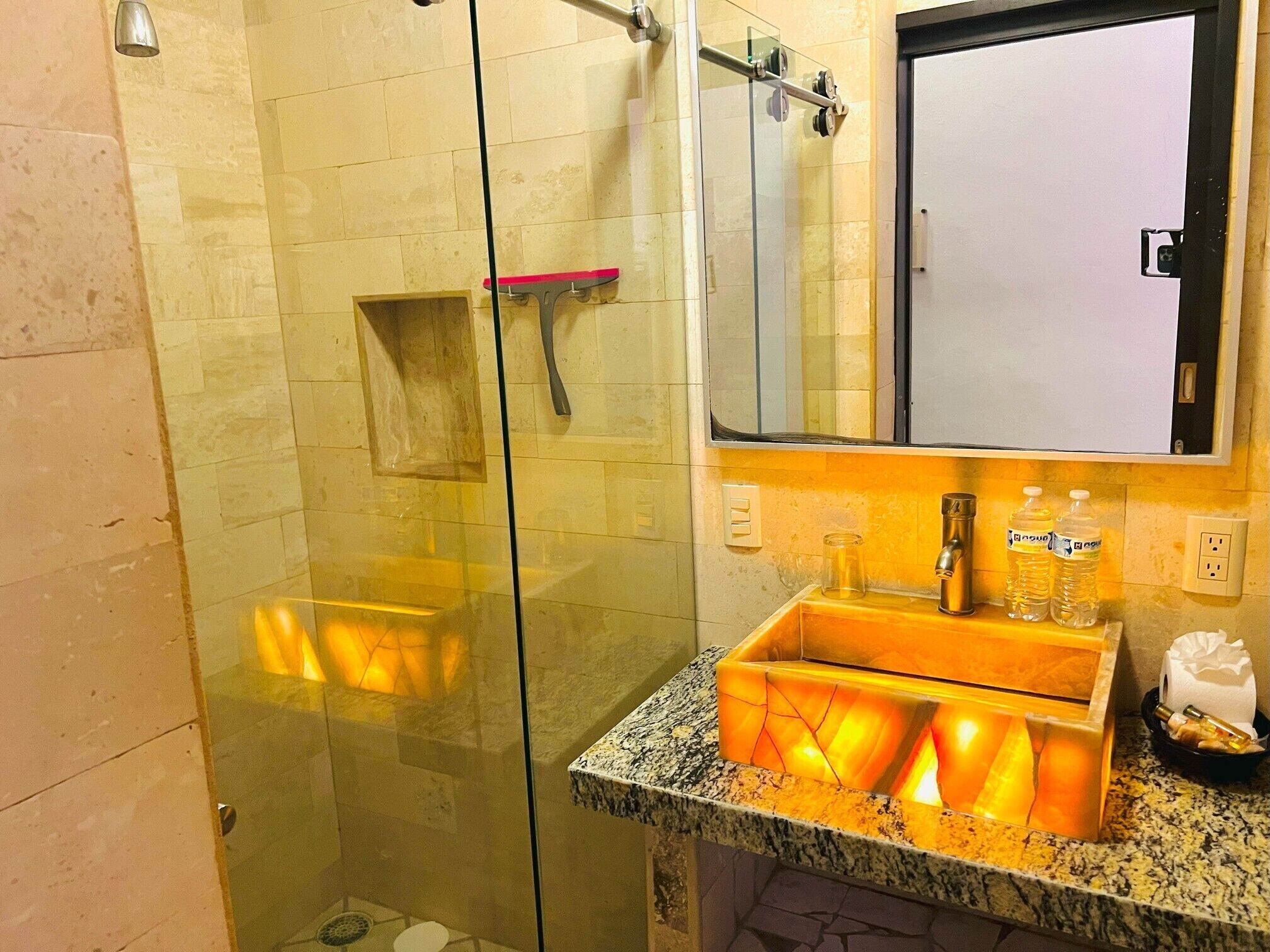 Un baño con cabina de ducha de vidrio, tocador con encimera de mármol y espejo sobre el lavabo.