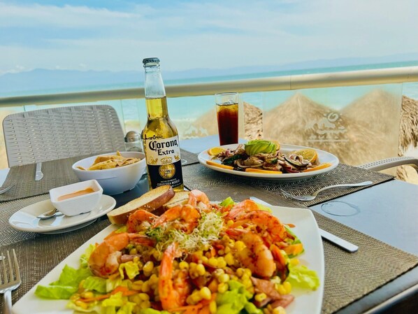 A dining table with a plate of shrimp and corn salad, a bottle of Corona beer, a glass of iced tea, and a bowl of soup. - Los Picos Hotel & Suites Bucerias (Bucerías)