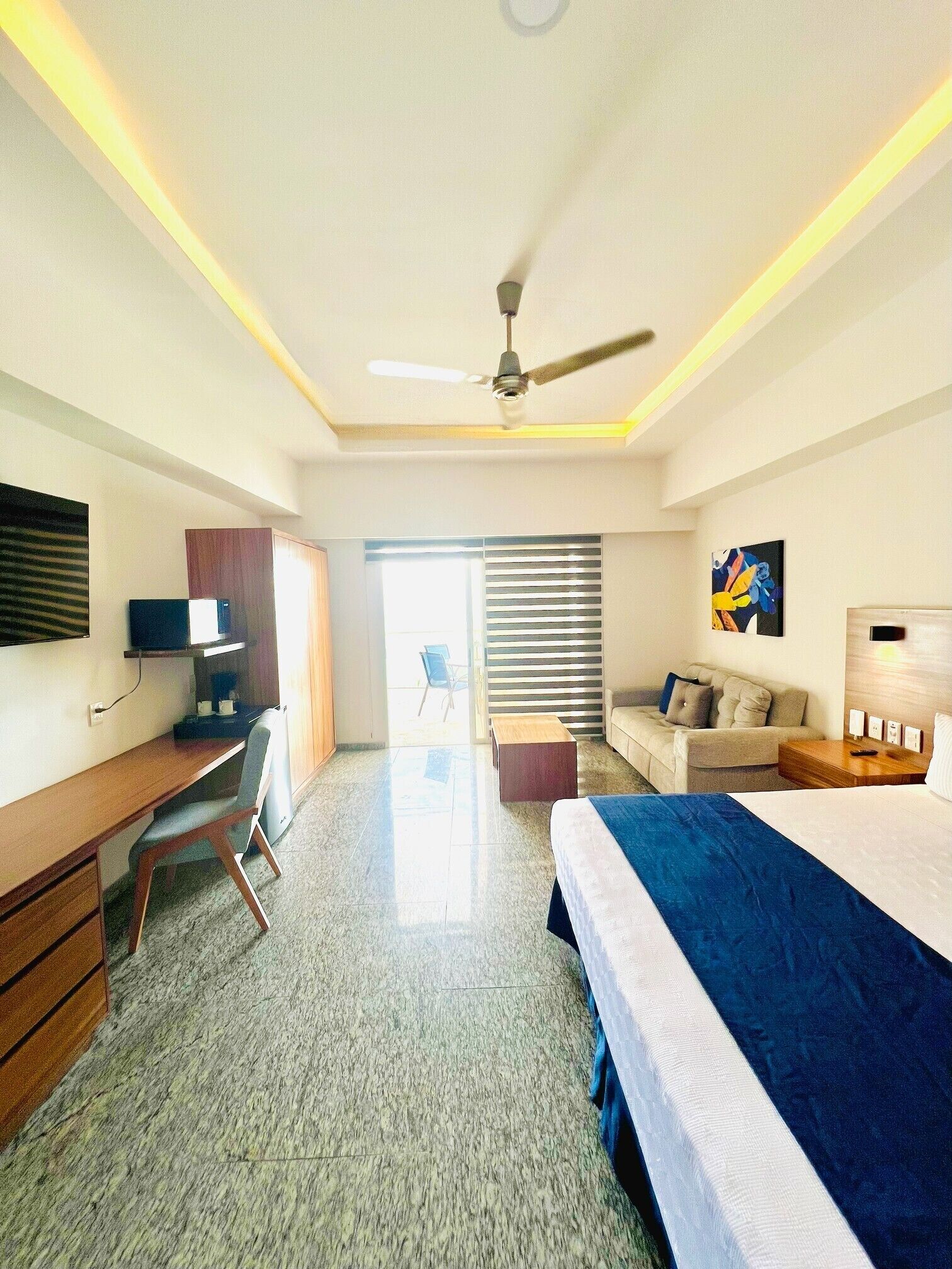 A hotel room with a bed, desk, chair, and a ceiling fan.