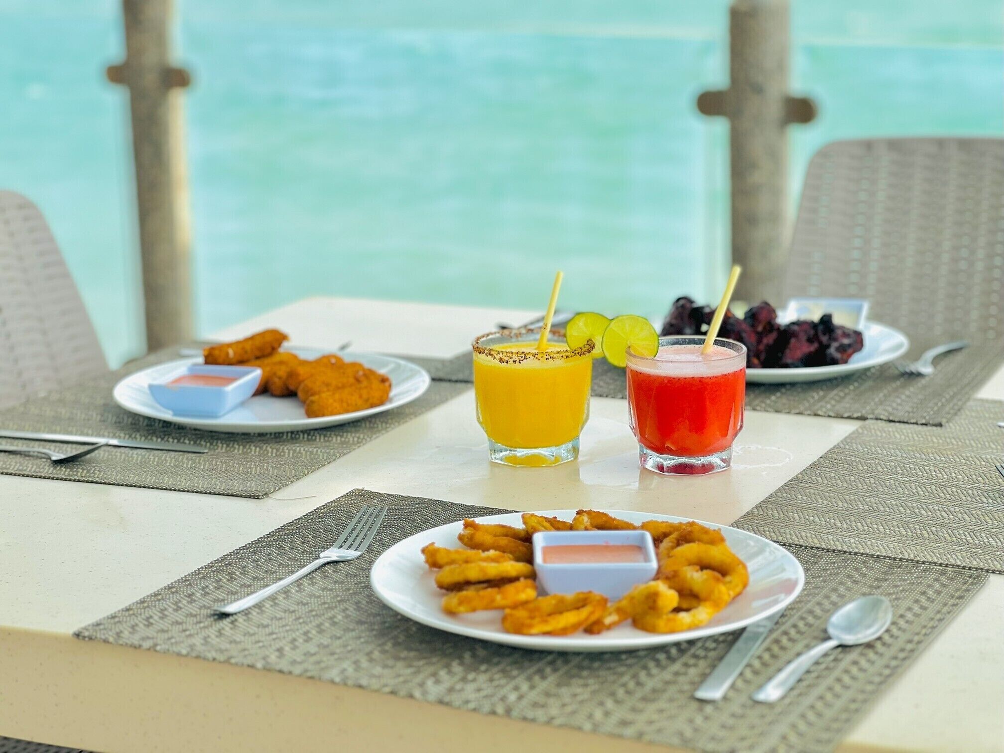 Ein Tisch mit gebratenem Essen, zwei Getränke und Blick aufs Meer.