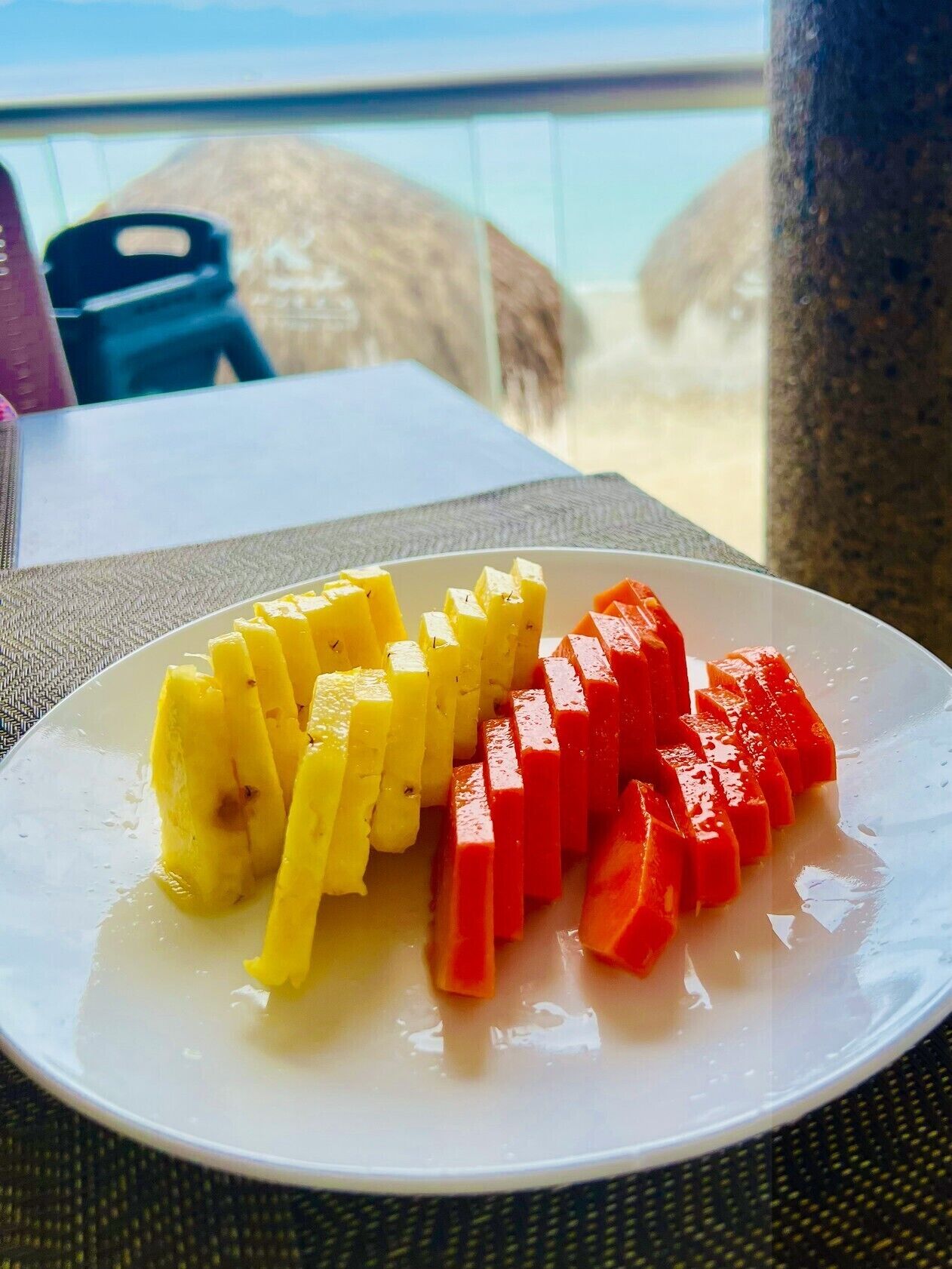 A plate of yellow and red fruit on a table with a view of the sea.