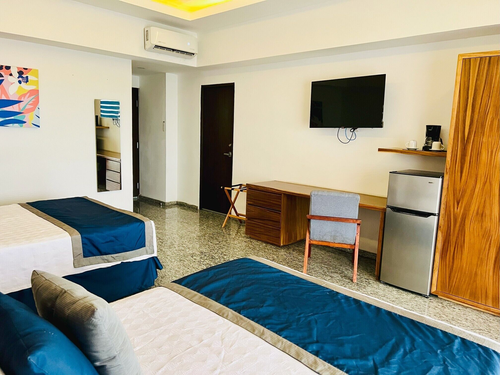 A hotel room with two beds, a desk, a TV, and a refrigerator.