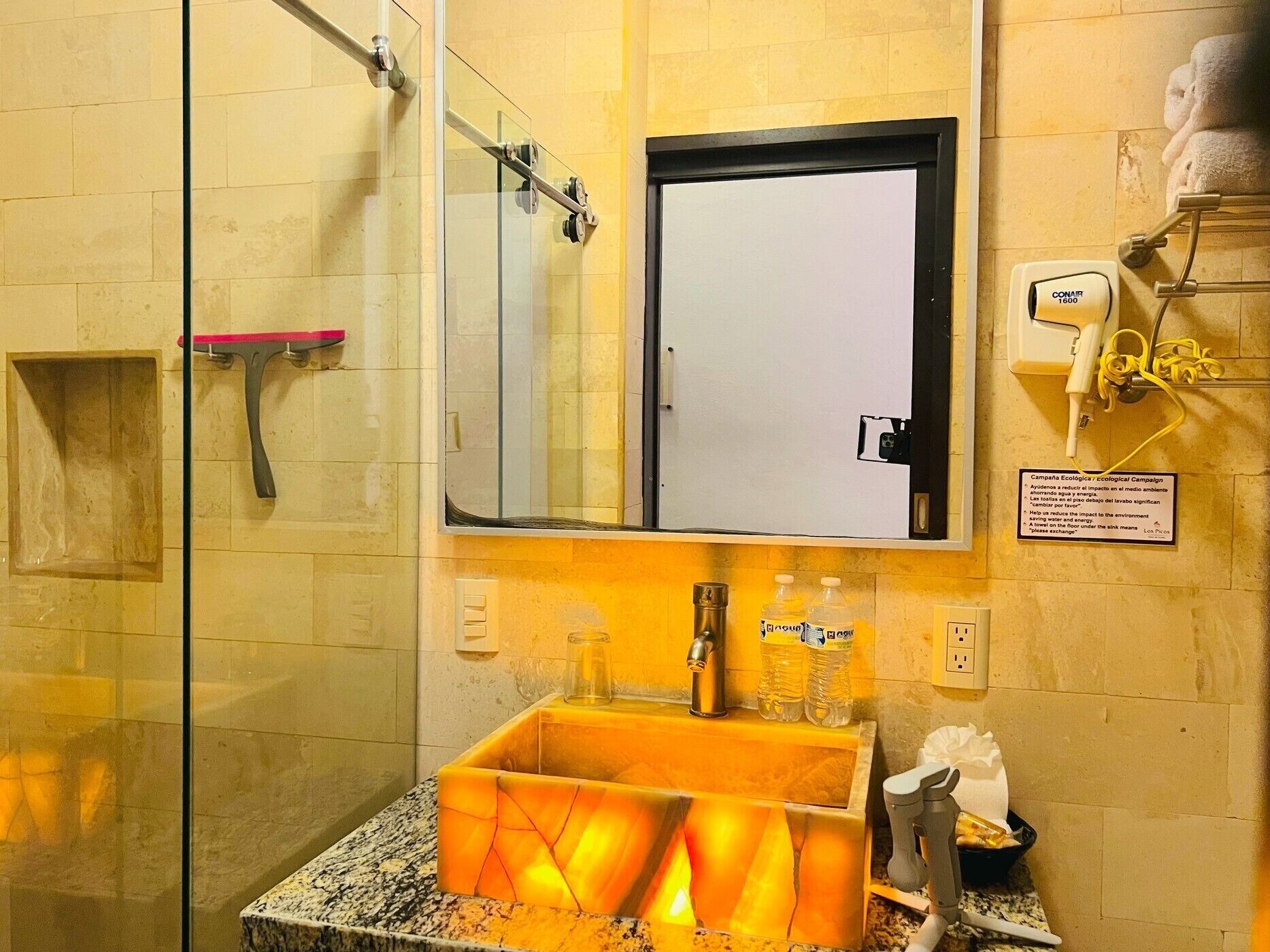 A bathroom with a glass shower enclosure, a sink with a yellow soap dispenser, and a mirror above the sink.