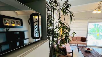 Una sala de estar moderna con una planta grande en maceta, un sofá, una mesa de centro y un televisor.