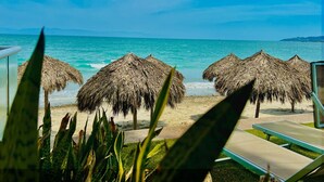 Vista sulla spiaggia con ombrelloni di paglia e poltroncine da spiaggia.