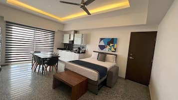 A modern hotel room with a bed, desk, and chair, a ceiling fan, and a painting on the wall.