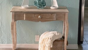 Een houten consoleschrank met twee witte modelzeilboten, een decoratieve groene plant en een witte plaid op een beige poef.