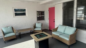 Een overdekt terras met rieten meubels, een tafeltje en een roze deur.