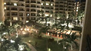 Ein Hotelinnenhof bei Nacht mit beleuchteten Wegen, Palmen und einem Poolbereich.